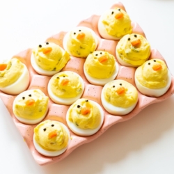 Deviled eggs made into little Easter chicks, on a pink ceramic egg holder.