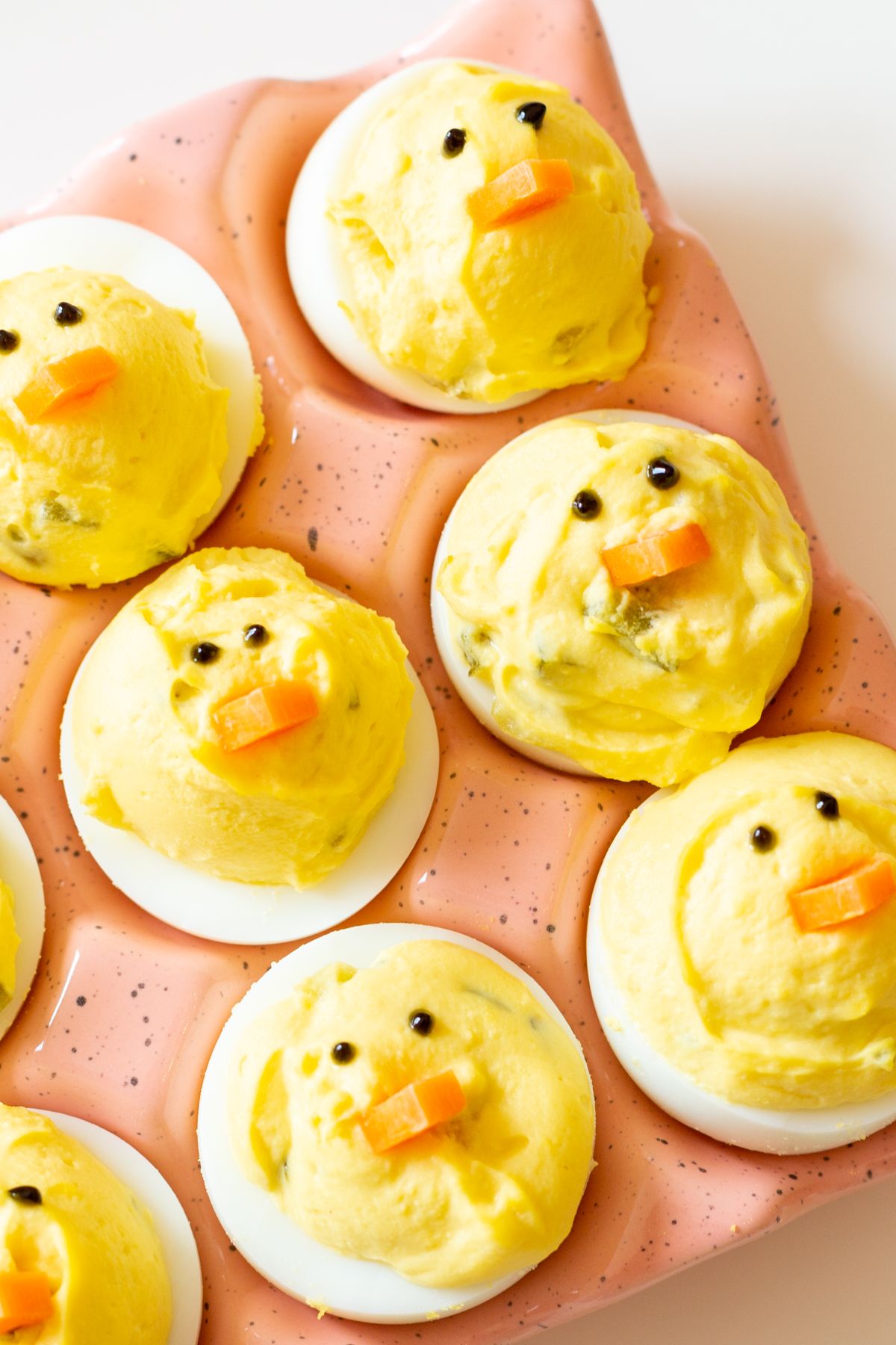 Deviled eggs made into little Easter chicks, on a pink ceramic egg holder.