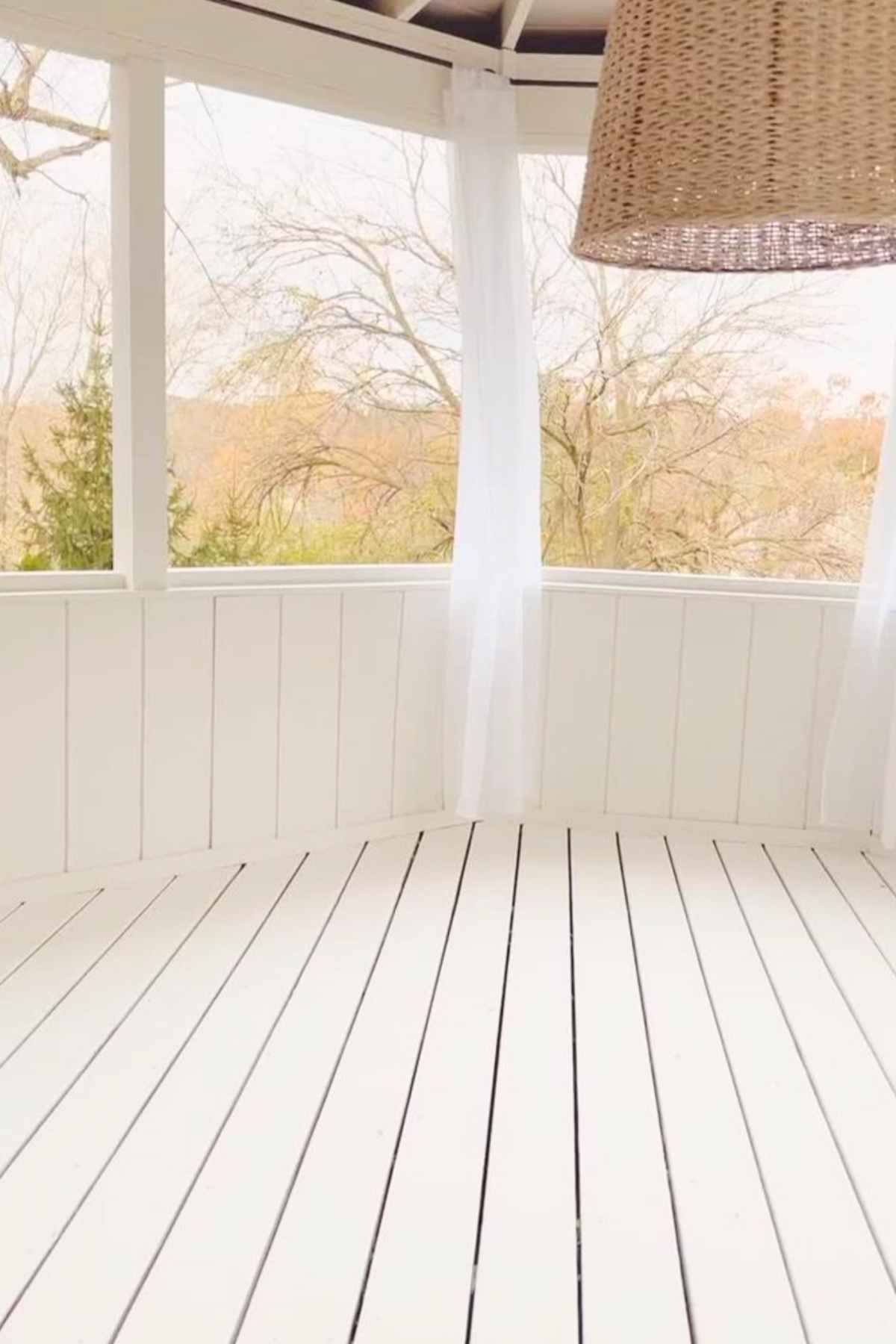 A screened in porch with a seagrass pendant light, hanging over wooden floors painted with deck paint. 