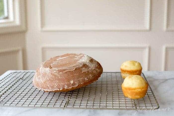 A round cake and two small cupcakes on a cooling rack on a marble surface.