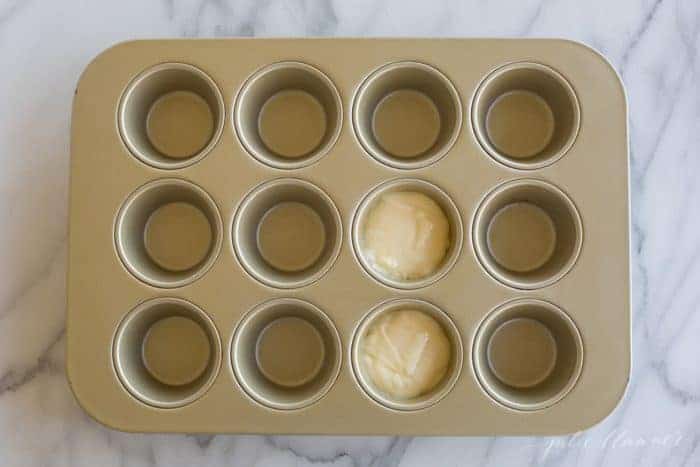 A gold muffin tin with two muffin spaces filled with cake mix.