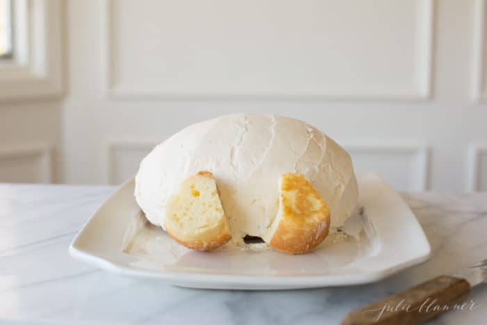 A round cake frosted in white frosting on a white platter to make an Easter Bunny Cake.