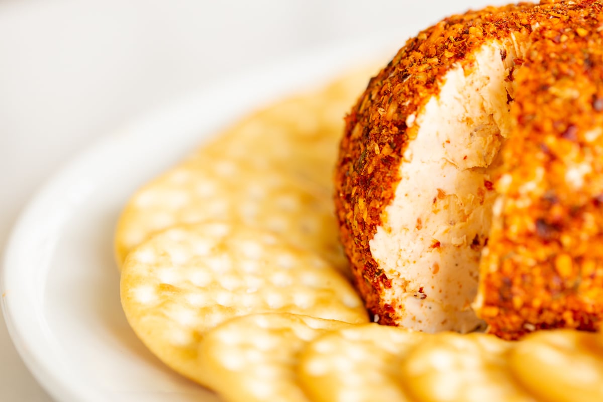 A spicy cheese ball on a white plate surrounded by crackers.