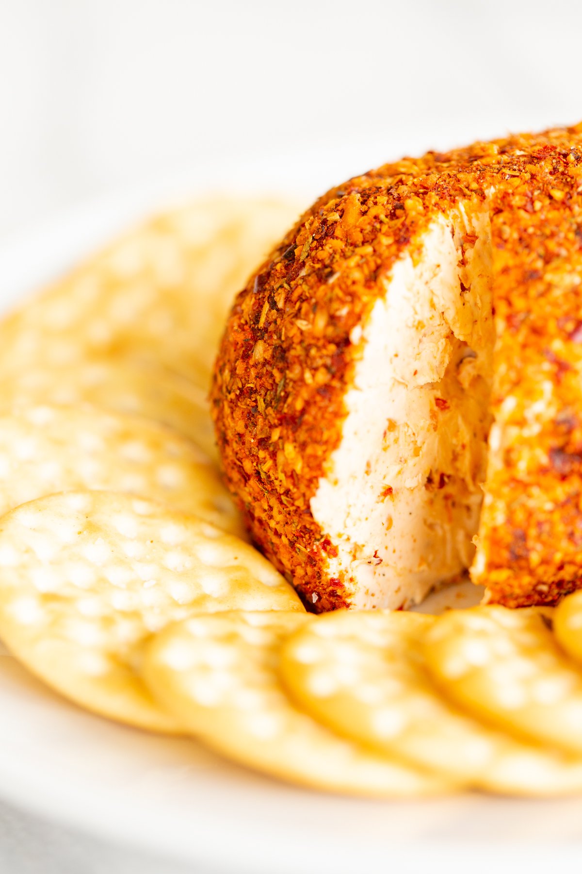 A spicy cheese ball on a white plate surrounded by crackers.