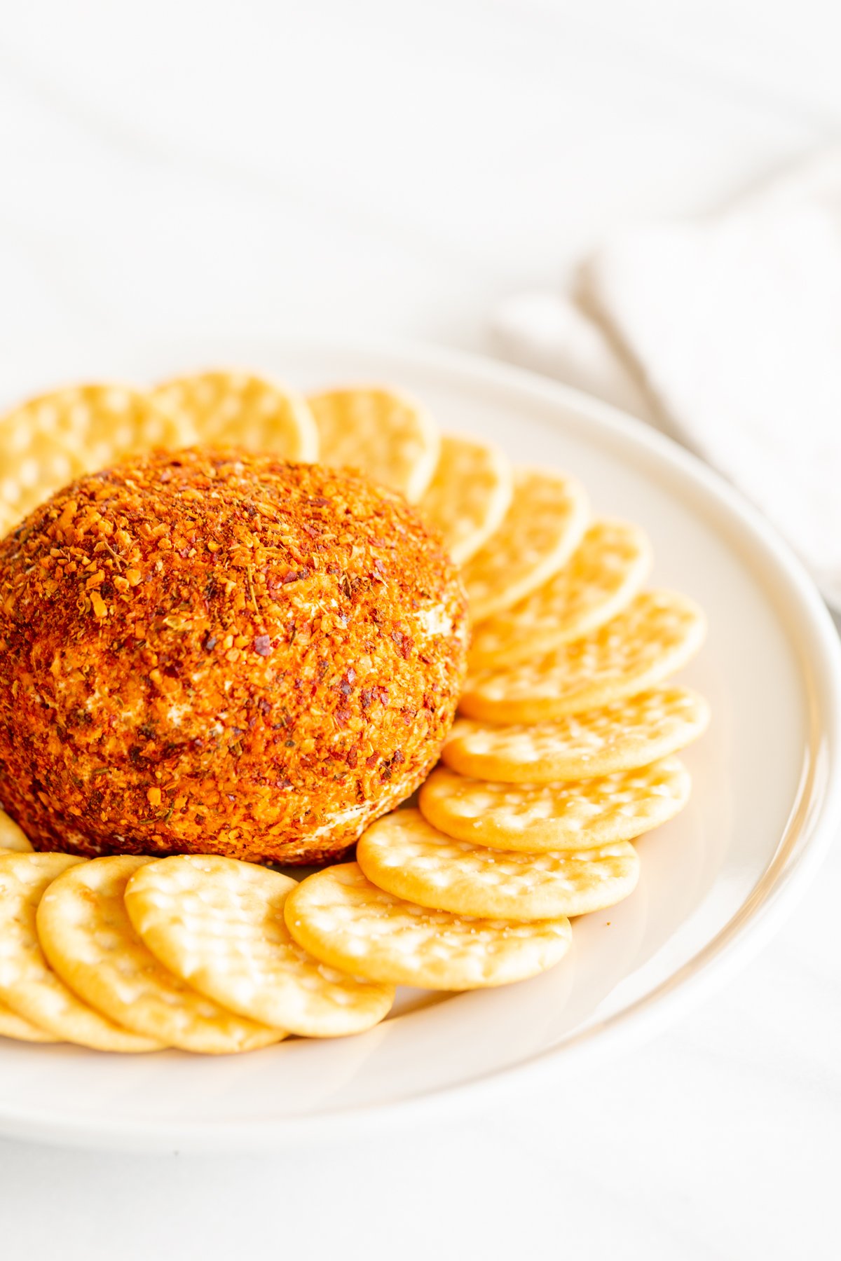 A spicy cheese ball on a white plate surrounded by crackers.