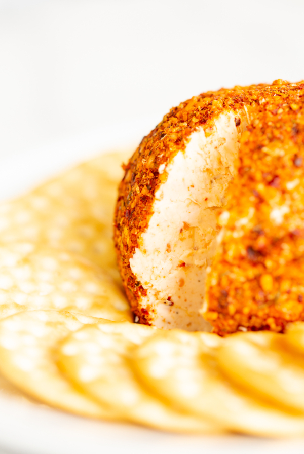 A spicy cheese ball on a white plate surrounded by crackers.