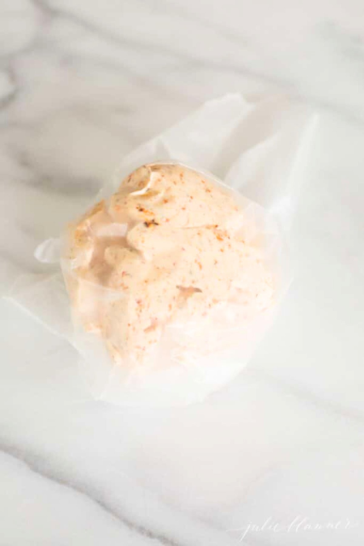 A spicy cheese ball wrapped in plastic wrap on a marble countertop.