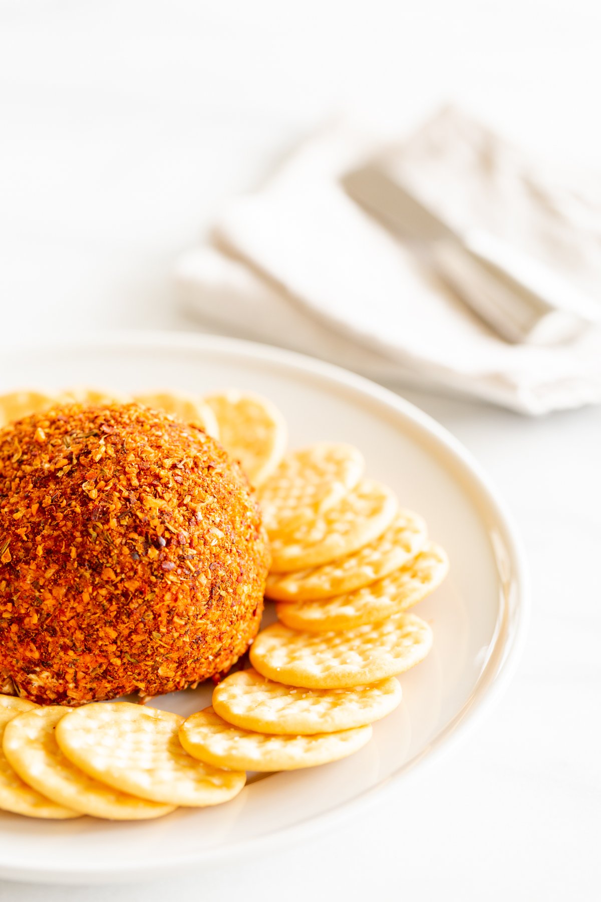 A spicy cheese ball on a white plate surrounded by crackers.