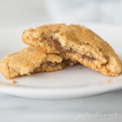 A white plate with a chocolate stuffed peanut butter cookie split into two halves.