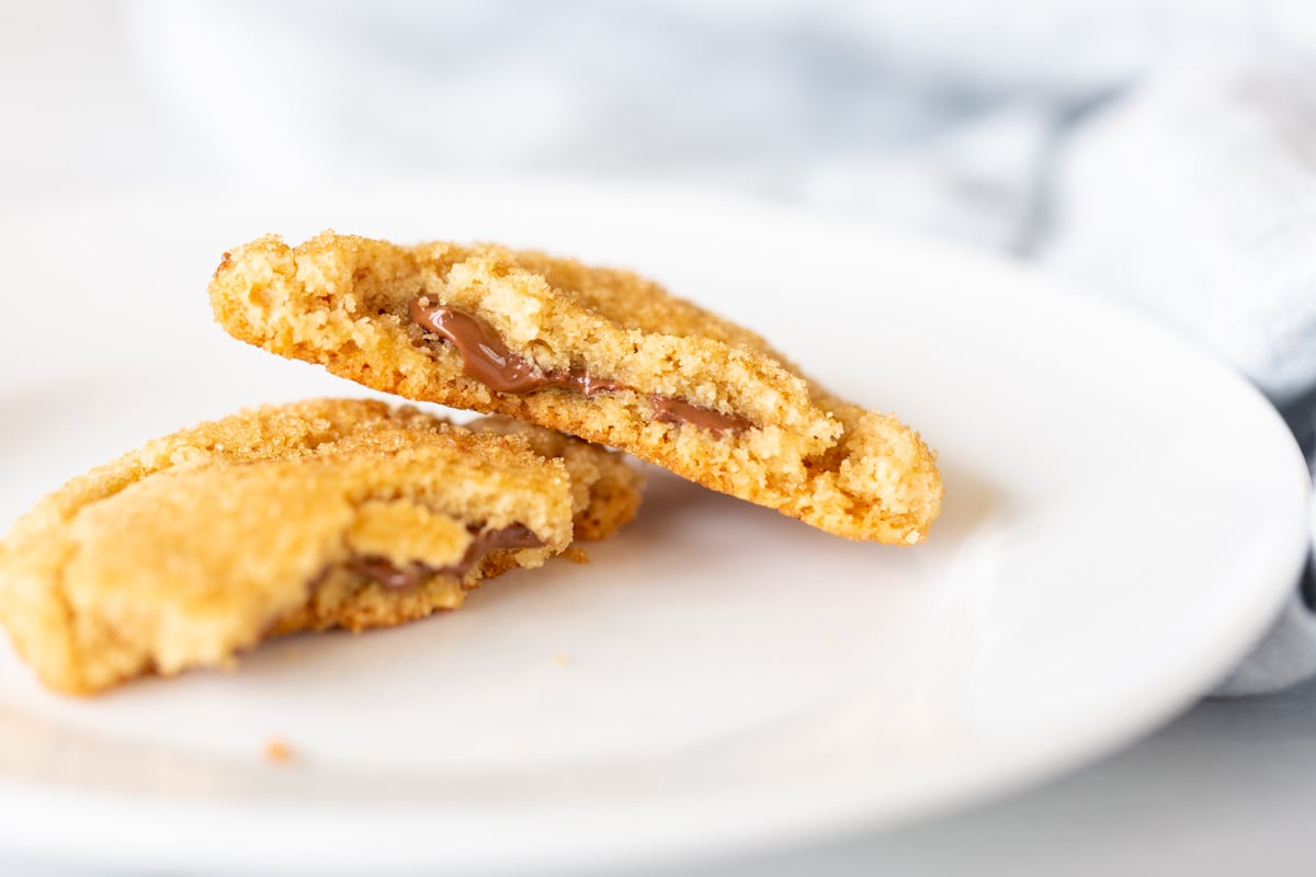 A white plate with a chocolate stuffed peanut butter cookie split into two halves.