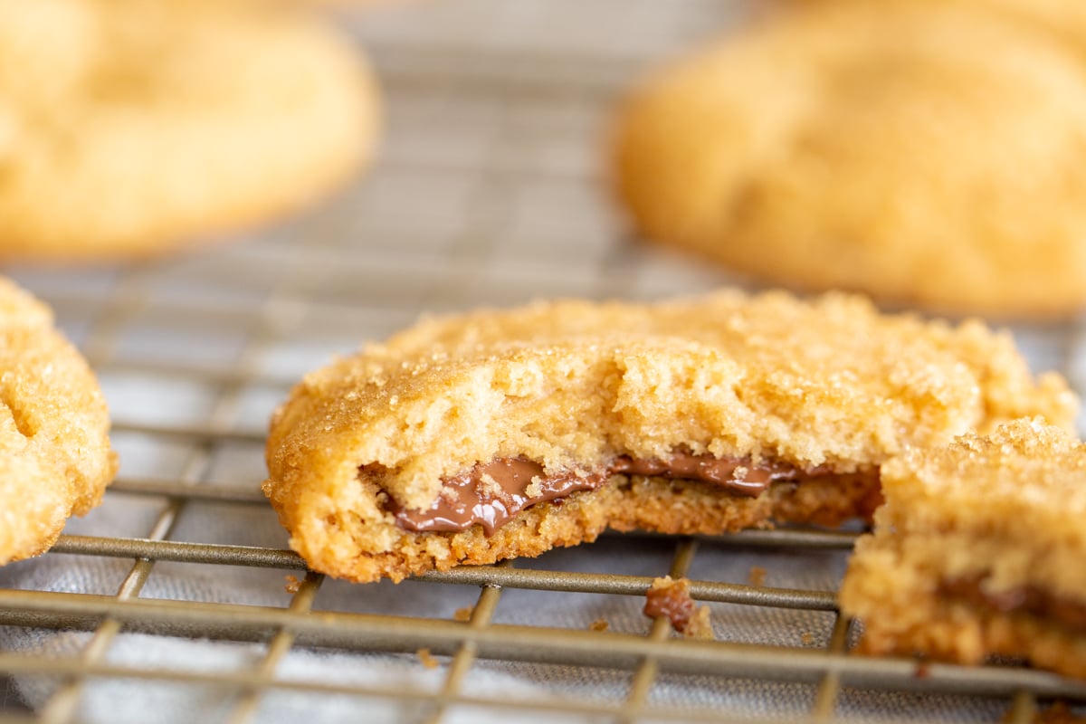 A cooling rack with a chocolate stuffed peanut butter cookie split into two halves.