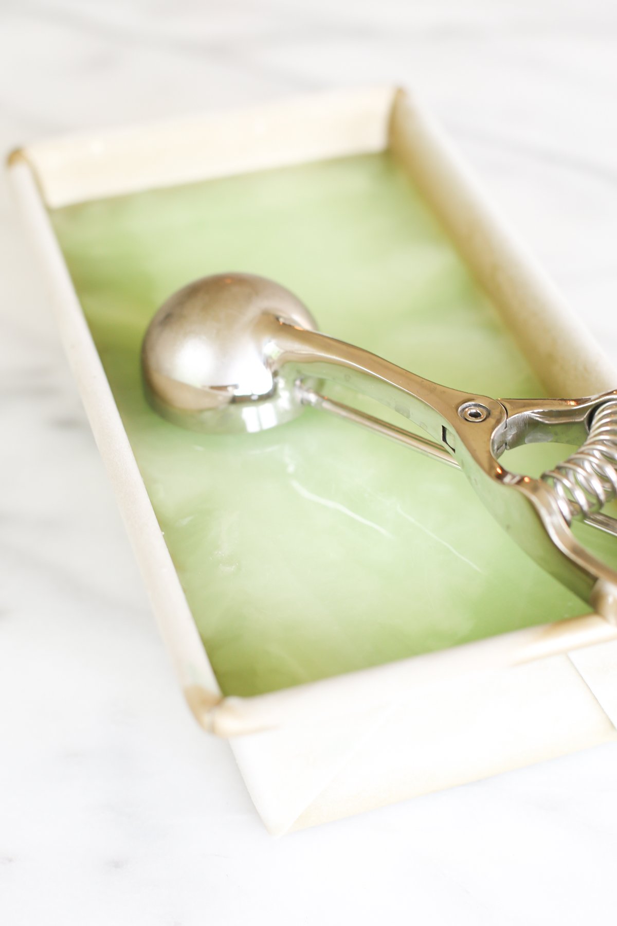 Homemade lime sorbet in a gold loaf pan with an ice cream scooper on top.