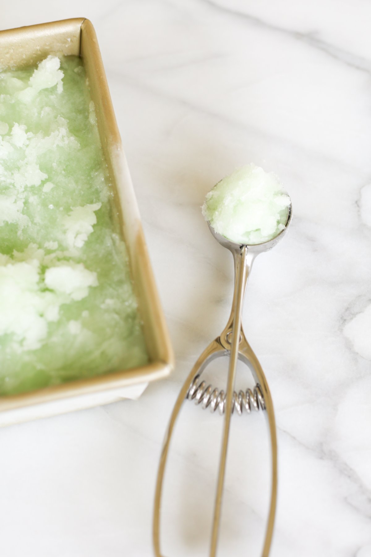 Homemade lime sorbet in a gold loaf pan. An ice cream scooper is nearby.