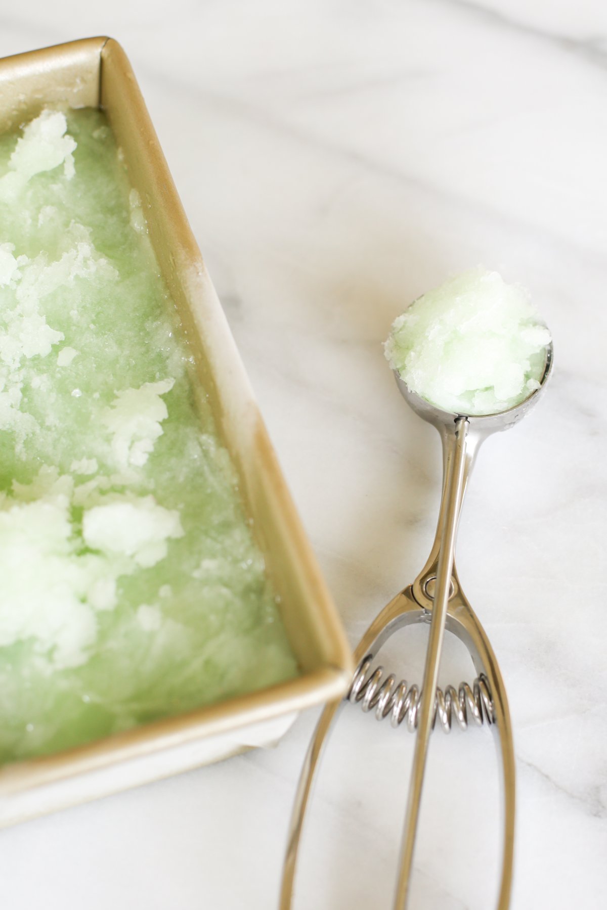 Homemade lime sorbet in a gold loaf pan. An ice cream scooper is nearby.