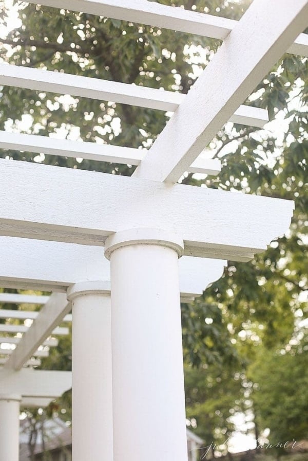 A white pergola attached to house with a tree in the background