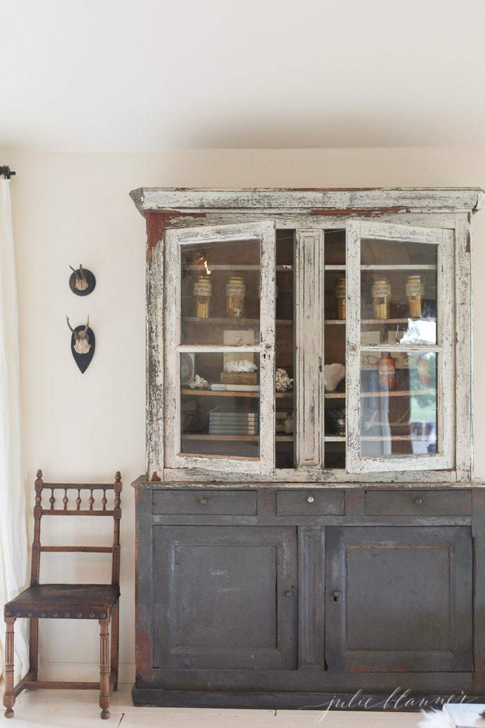 Simple European Farmhouse interior design with a rustic wood hutch and a simple chair to the side.