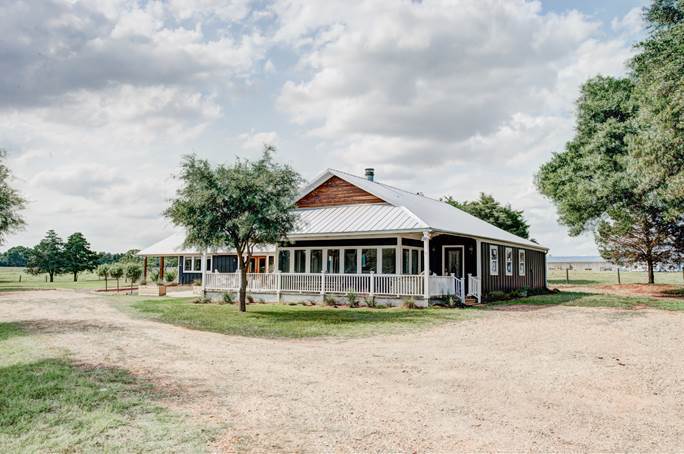 A charming Texas farmhouse with a white front porch and gravel driveway.