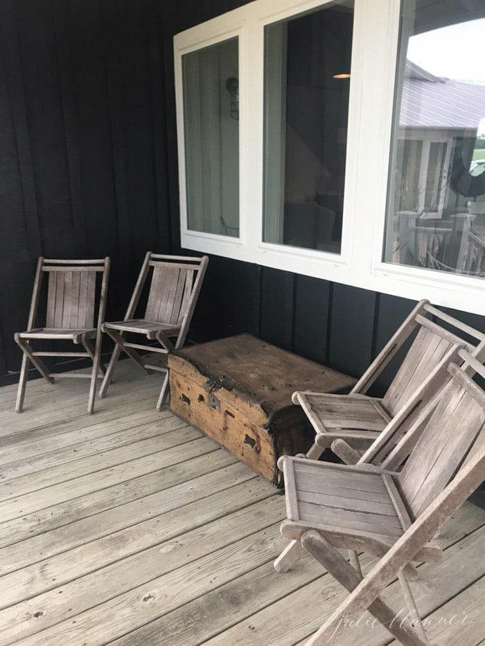 Urban farmhouse exterior with rustic wooden chairs and black siding, white windows.