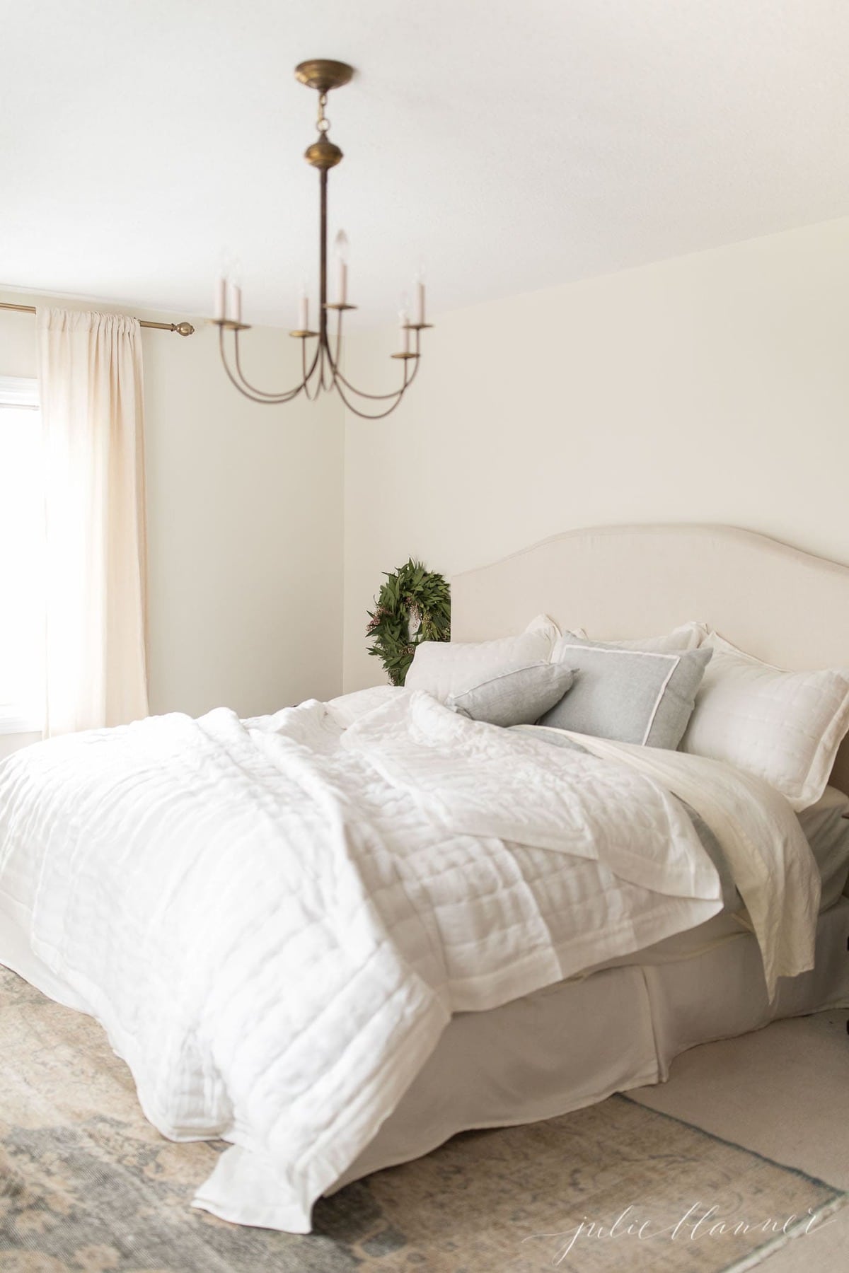 A cream bedroom with ivory curtains hanging on a brass curtain rod