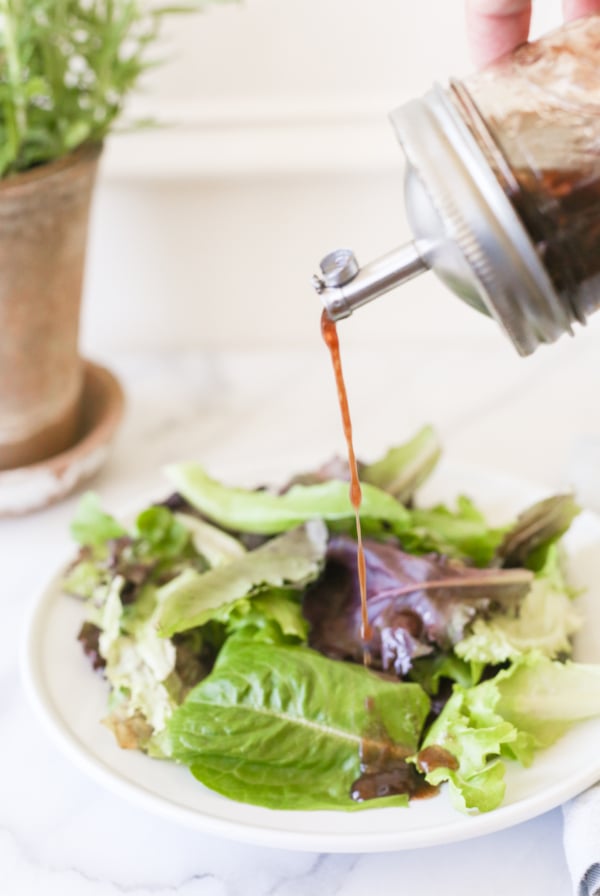 Balsamic vinaigrette in a glass bottle, pouring over a salad.