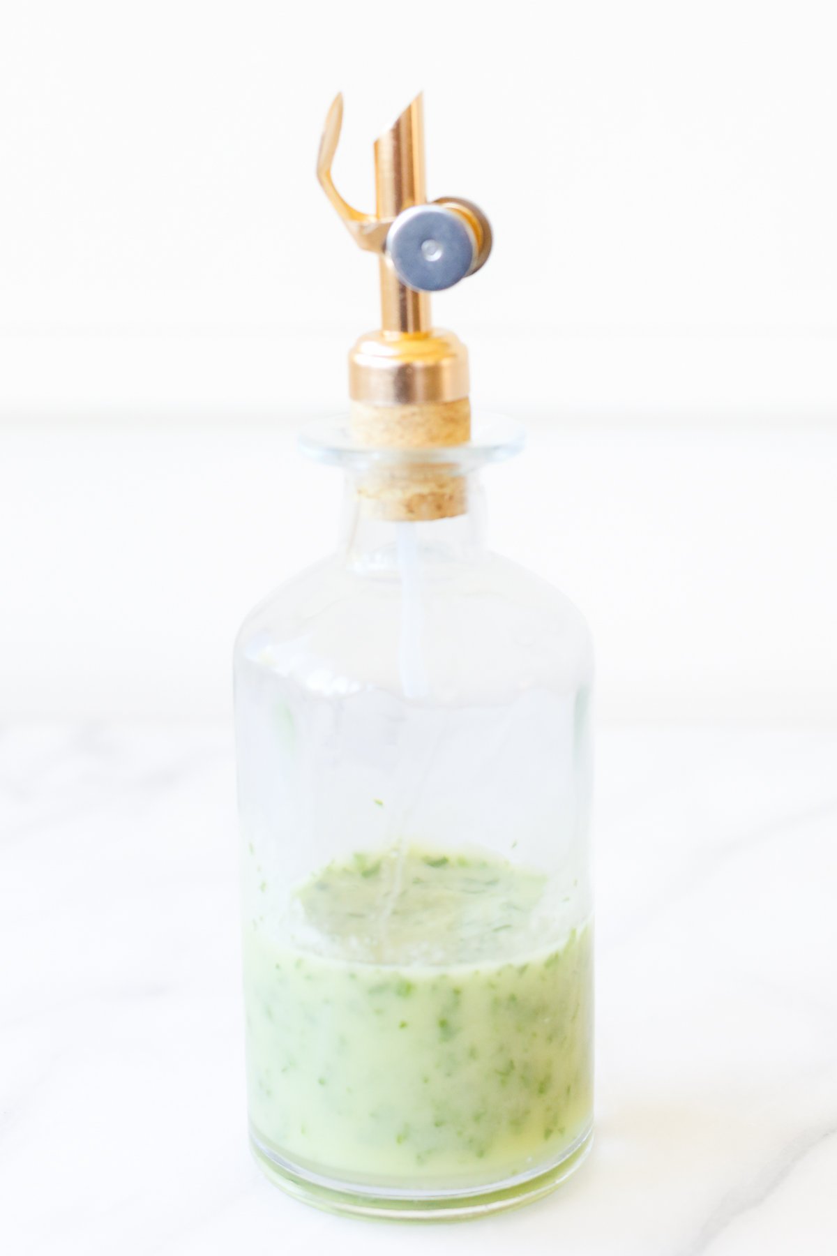 A clear glass bottle of a green herb vinaigrette.