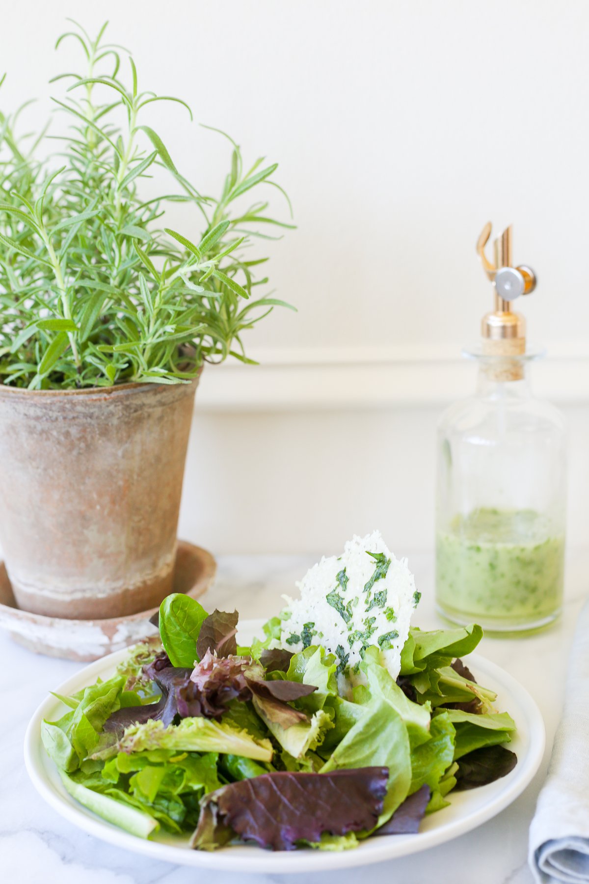 A leafy green salad on a white plate, with a glass bottle of herb vinaigrette in the background.