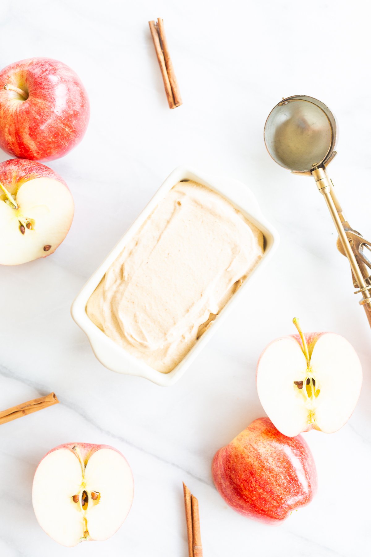 A bowl of delicious apple ice cream adorned with cinnamon sticks and fresh apples.