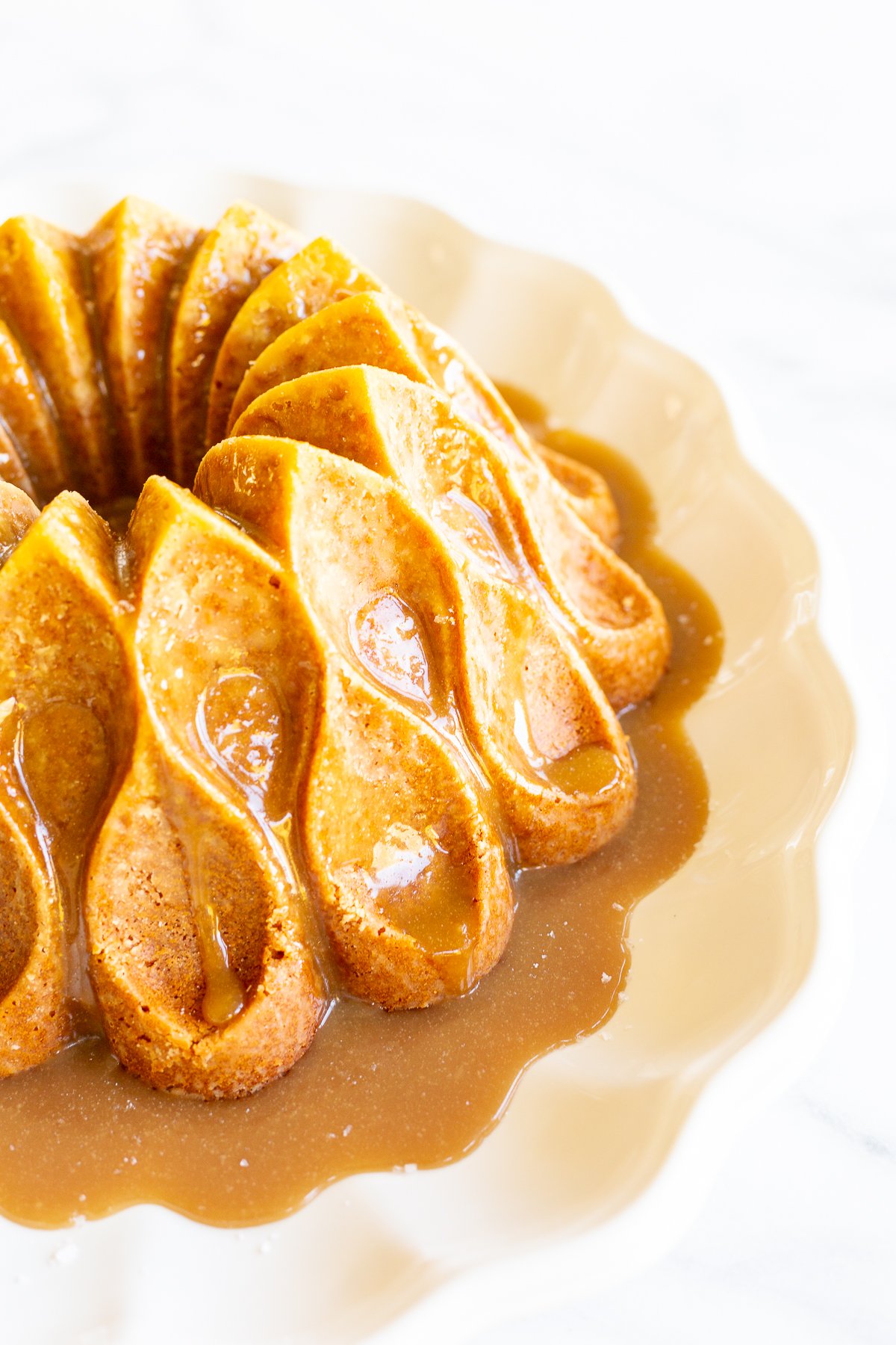 A brown sugar caramel pound cake on a white platter, baked in a bundt pan and topped with caramel sauce.