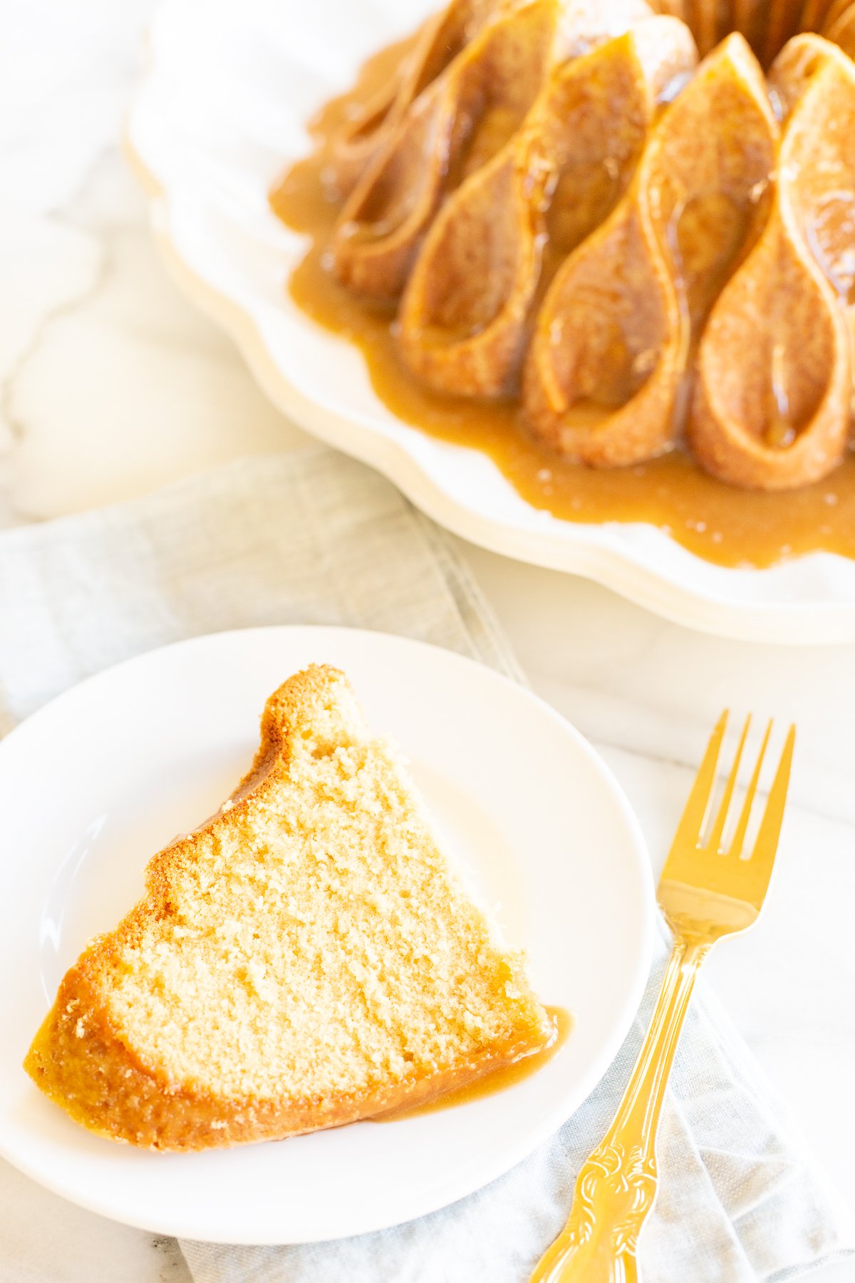 A slice of brown sugar caramel pound cake on a white plate, with the bundt cake in the background.