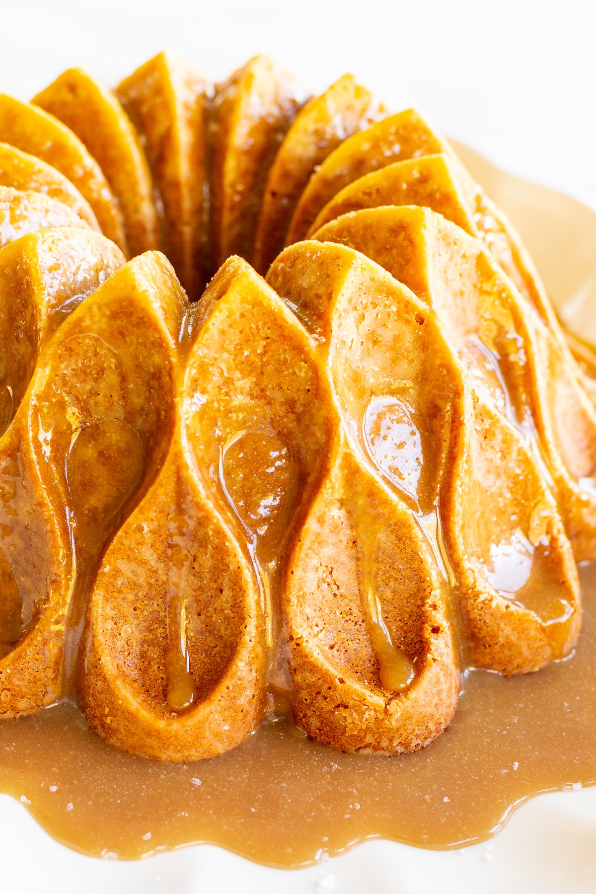 A brown sugar caramel pound cake on a white platter, baked in a bundt pan and topped with caramel sauce.