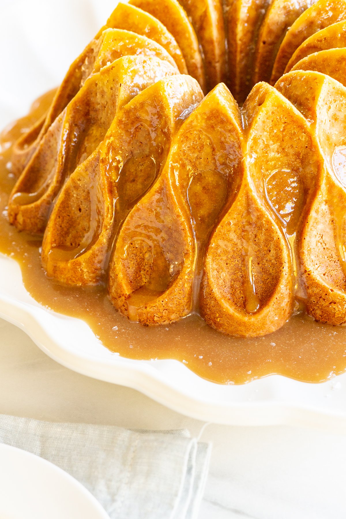 A brown sugar caramel pound cake on a white platter, baked in a bundt pan and topped with caramel sauce.