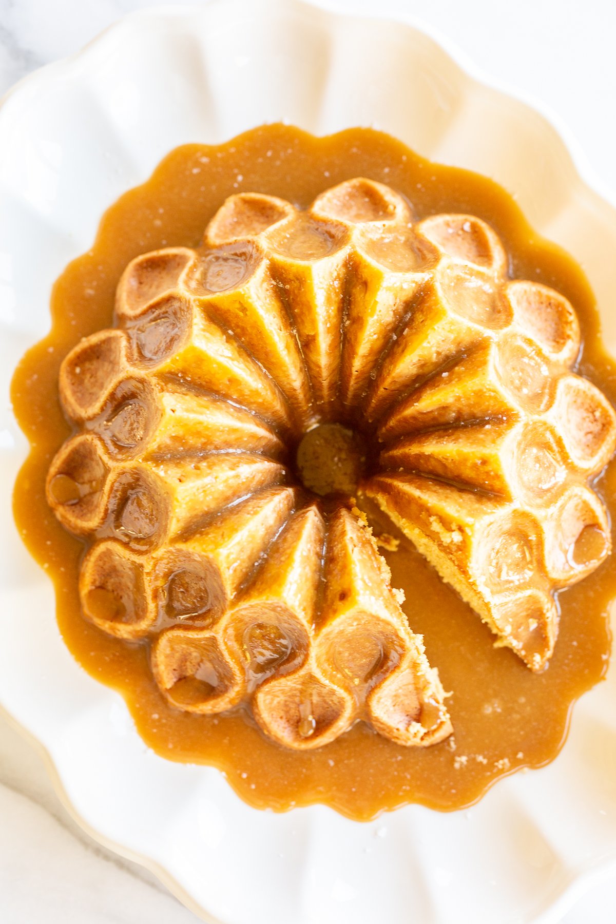 A brown sugar caramel pound cake on a white platter, baked in a bundt pan and topped with caramel sauce.