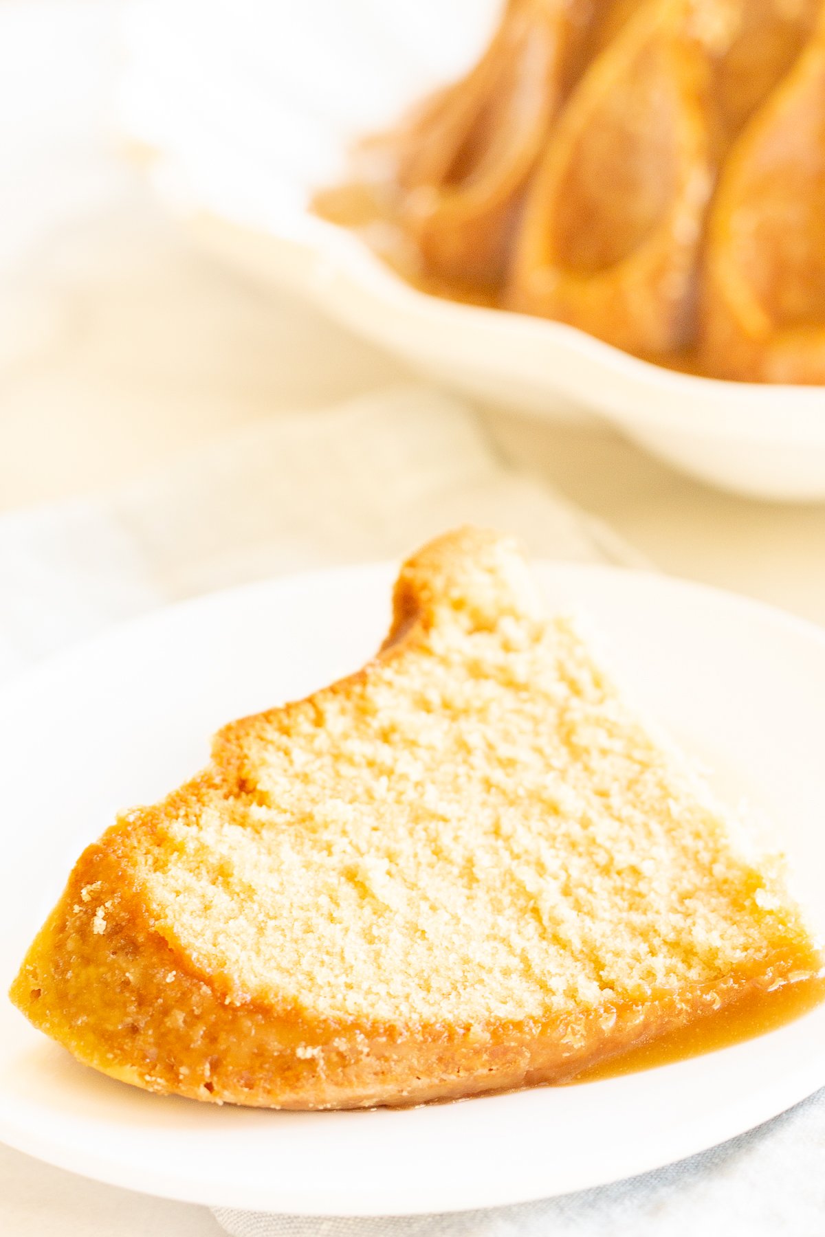 A slice of brown sugar caramel pound cake on a white plate, with the bundt cake in the background.