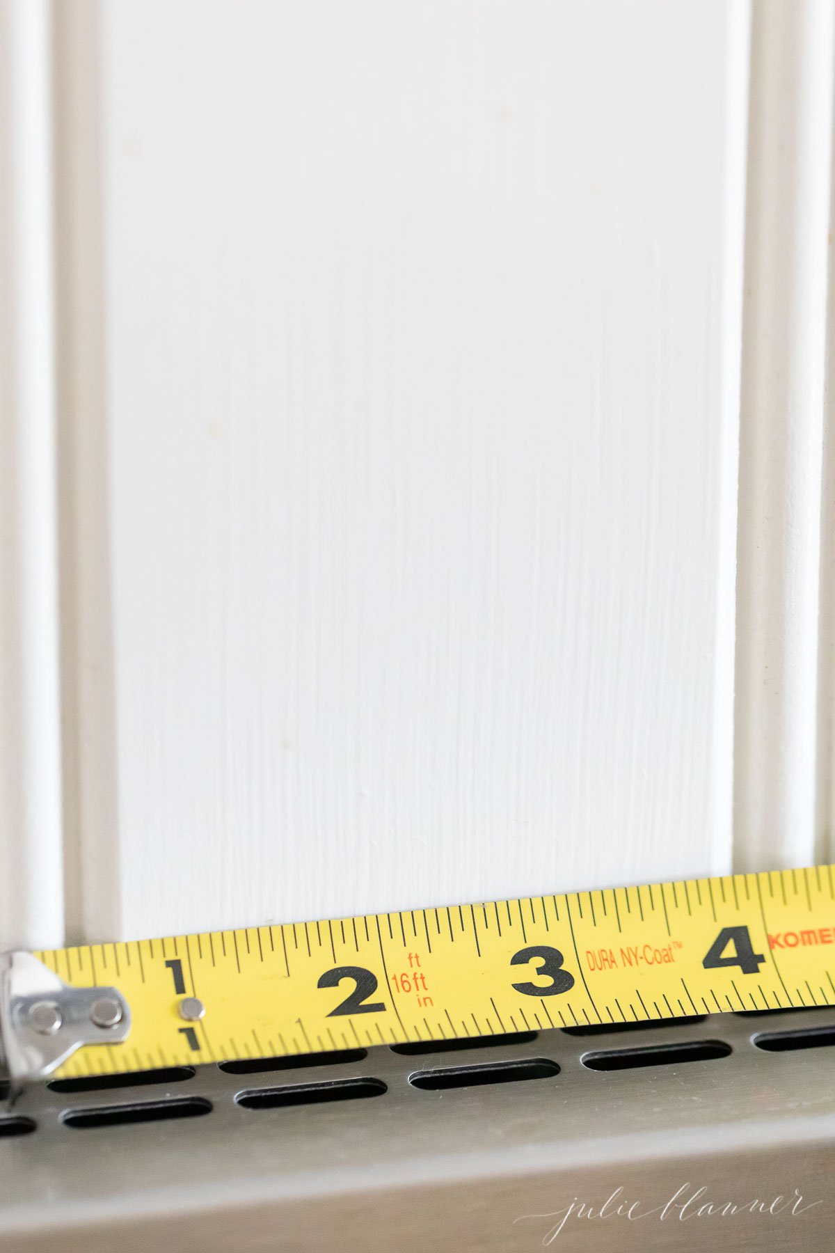 A measuring tape next to a white beadboard backsplash.