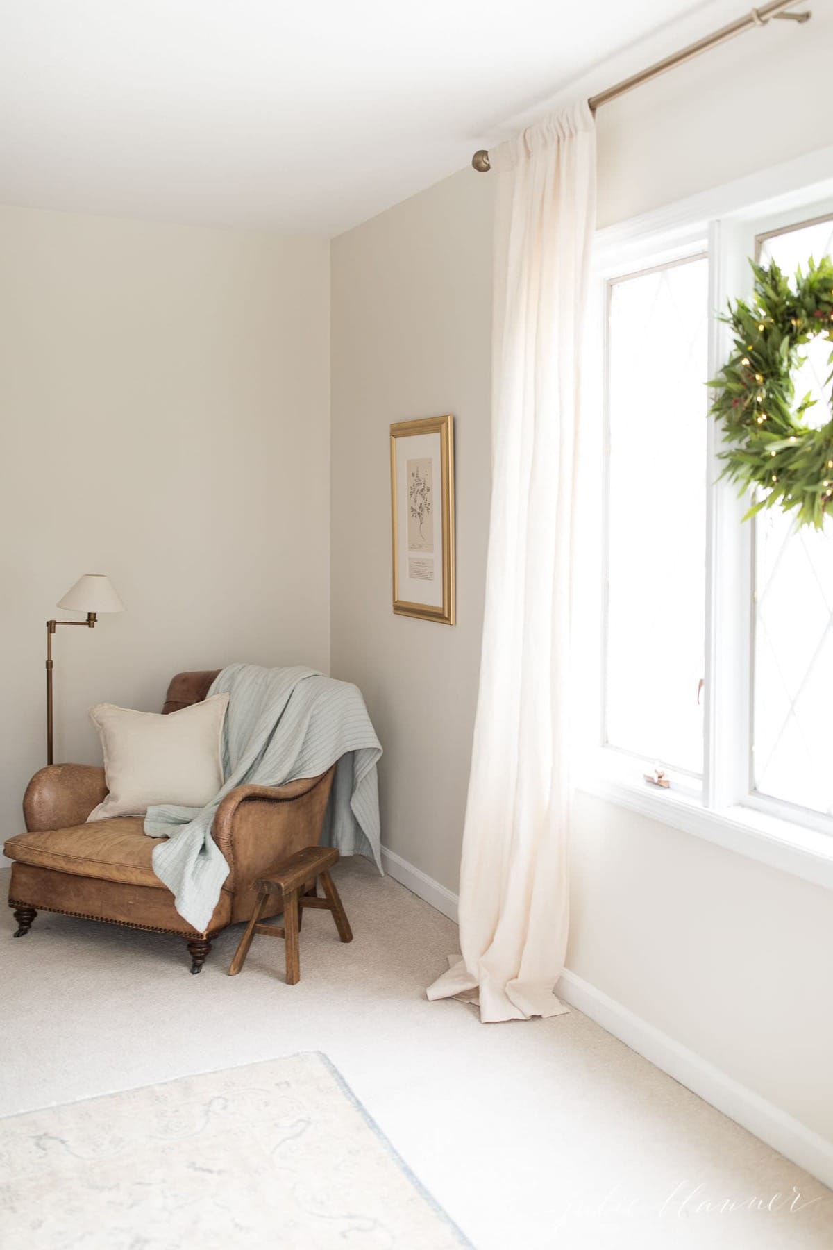 A beige living room with a chair and a wreath incorporating Christmas lights.