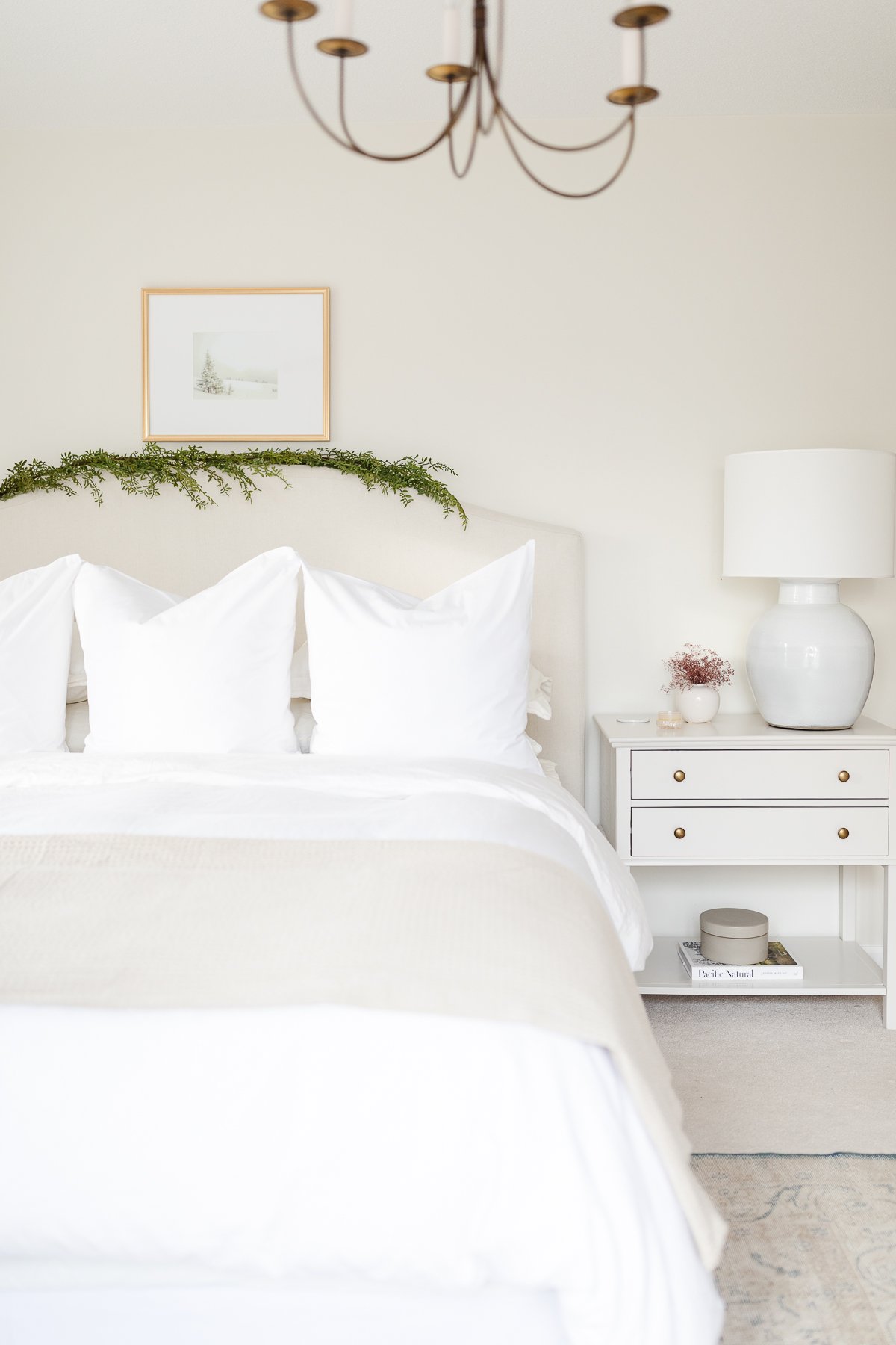 A bedroom with white bedding and Christmas lights.