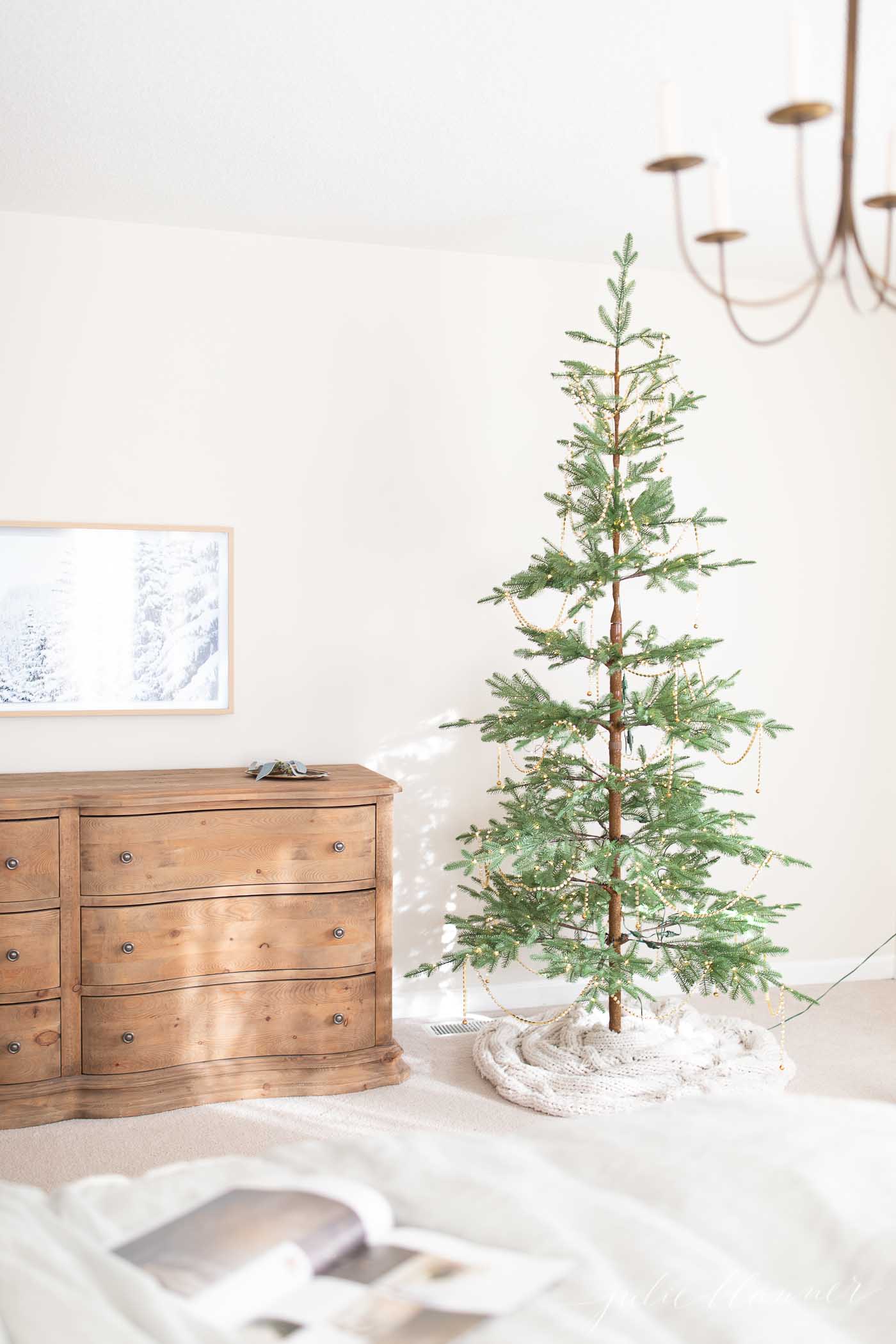 A cozy bedroom adorned with a Christmas tree and a dresser, illuminated by enchanting Christmas lights.