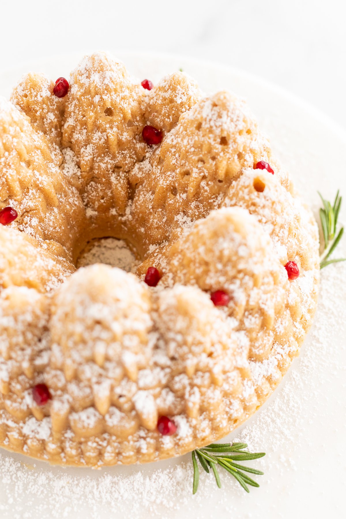 A cinnamon pound cake topped with powdered sugar and a sprig of rosemary.