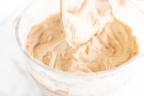 A person carefully pouring creamy peanut butter into a bowl to complement their delicious cinnamon pound cake.