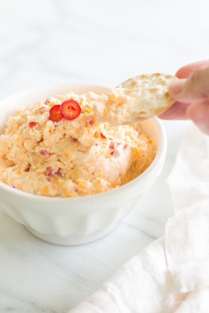 cracker being dipped into pimento cheese recipe in a white bowl