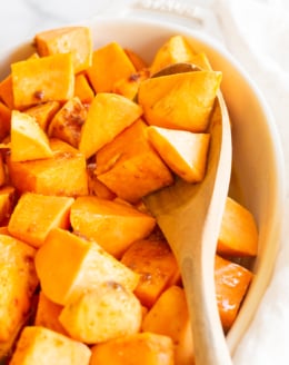 A white oval baking dish filled with roasted sweet potatoes.