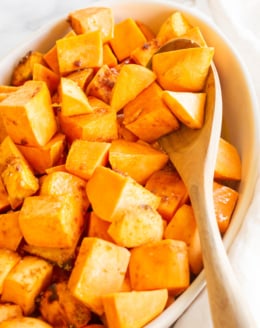 A white oval baking dish filled with roasted sweet potatoes.