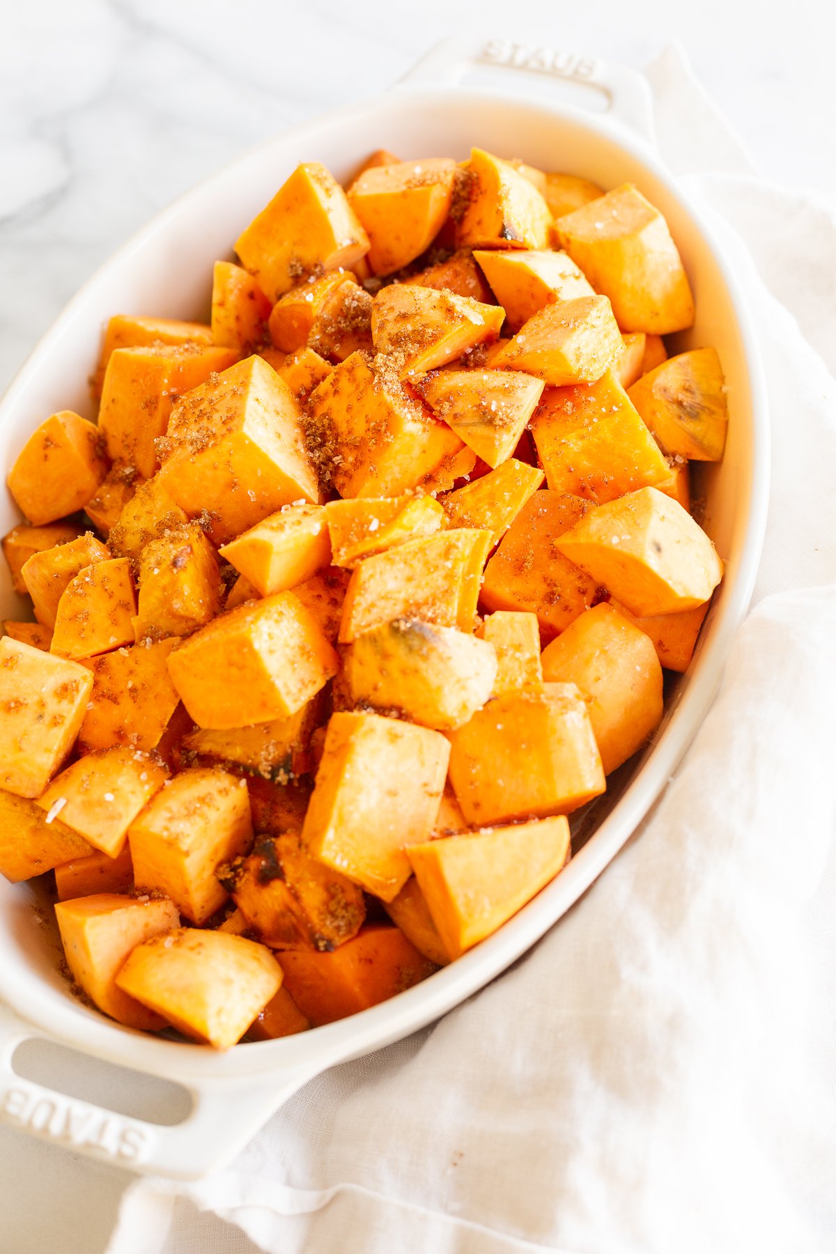 A white oval baking dish filled with roasted sweet potatoes.