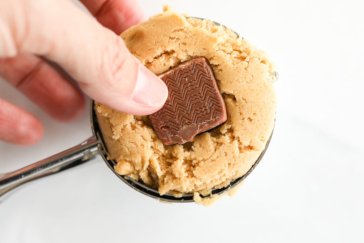 A person holding a spoon with a stuffed peanut butter cookie in it.