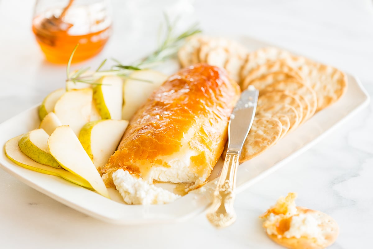 Baked goat cheese topped with honey with sliced pears and crackers for serving.