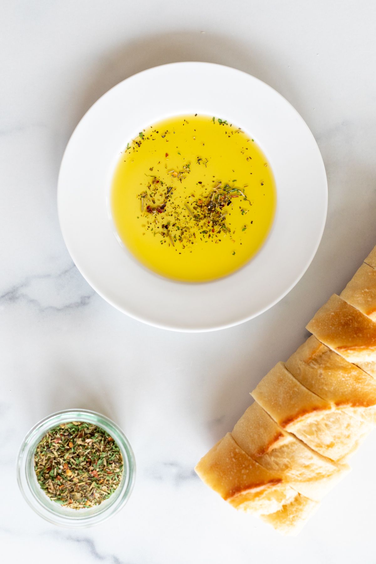 A white plate topped with bread dipping seasoning and olive oil, sliced bread in the background.