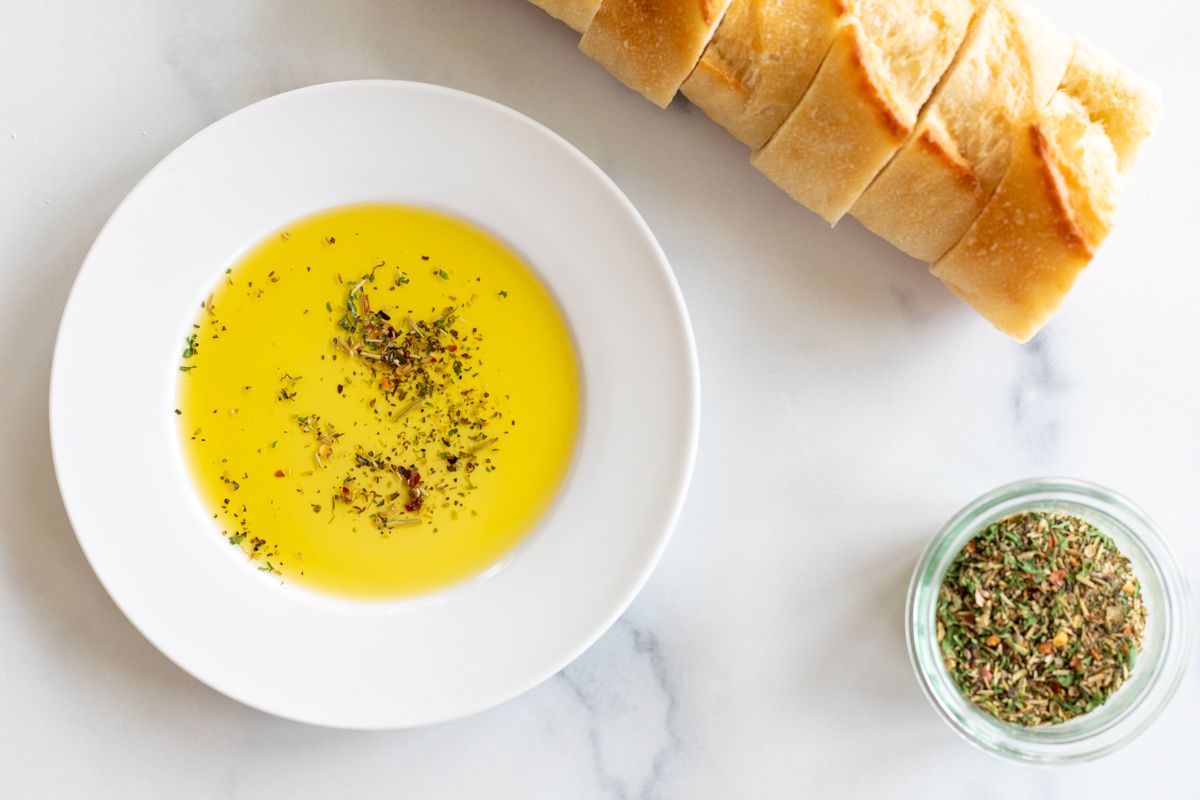 A white plate topped with bread dipping seasoning and olive oil, sliced bread in the background.