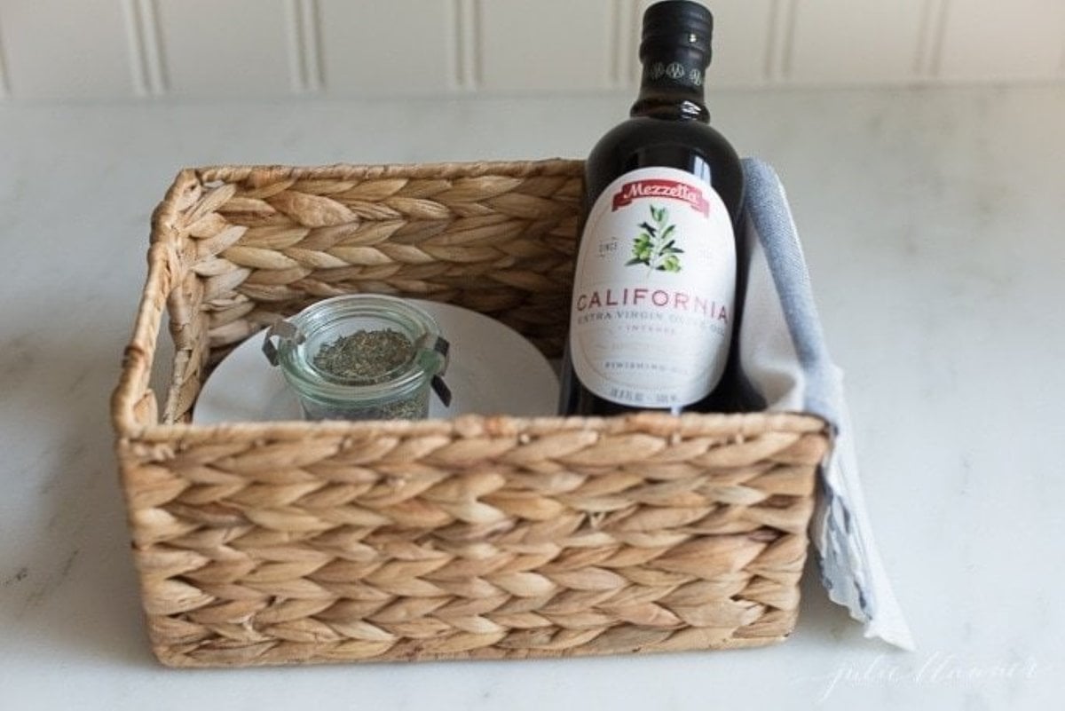 A gift basket with homemade bread dipping spices, a white plate and a bottle of olive oil. 