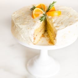 A mandarin orange cake on a cake stand, slice removed.