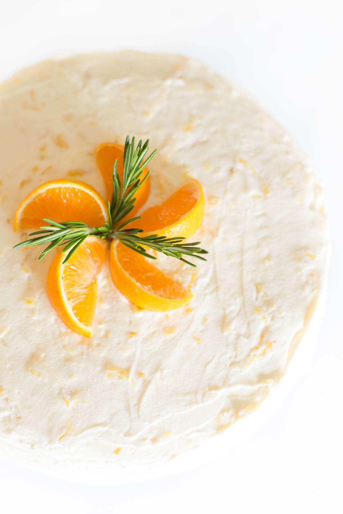 Sliced mandarin oranges and rosemary sprigs on top of a mandarin orange cake.